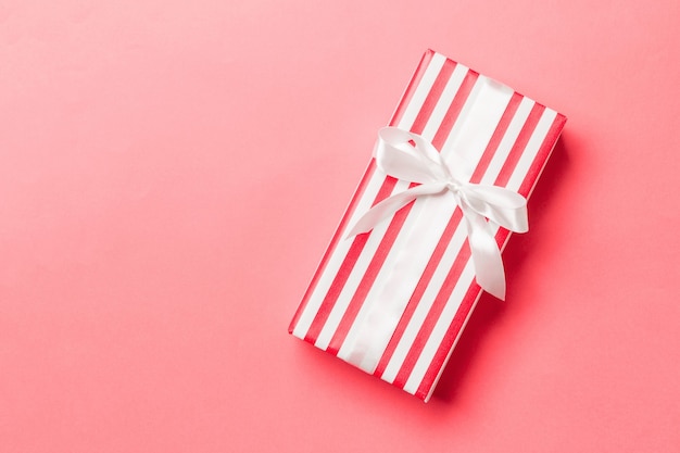 Top view Christmas present box with white bow on living coral background with copy space.