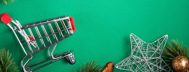 Vista dall'alto del concetto di design dello shopping natalizio con confezione regalo e carrello della spesa su sfondo verde tavolo