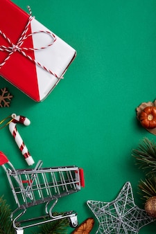 Vista dall'alto del concetto di design dello shopping natalizio con confezione regalo e carrello della spesa su sfondo verde tavolo