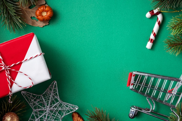 Vista dall'alto del concetto di design dello shopping natalizio con confezione regalo e carrello della spesa su sfondo verde tavolo Foto Premium