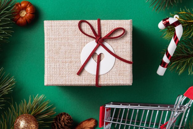 Вид сверху концепции дизайна рождественских покупок с подарочной коробкой и тележкой на зеленом фоне стола