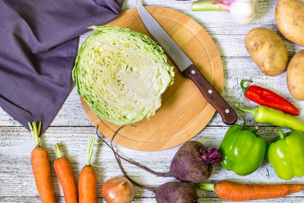 Top view of circle cutting board, knife and fresh vegetables on wooden table top