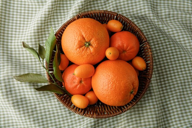 격자 무늬 천 배경에 바구니에 오렌지 귤과 금귤과 같은 감귤류 과일의 상위 뷰