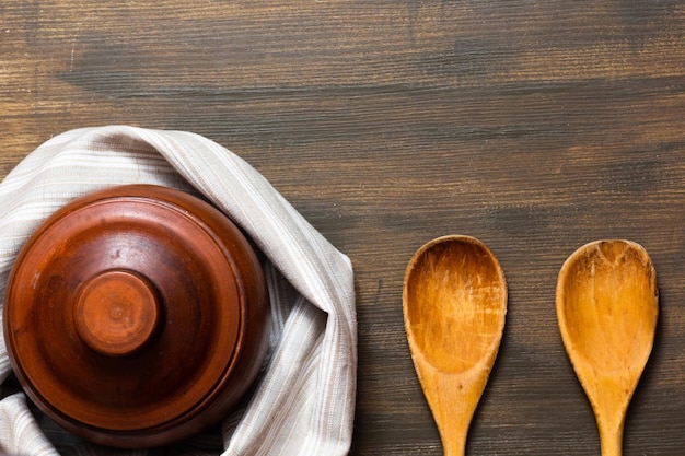 Top view of clay pot and wooden spoons on the wooden background with copy space
