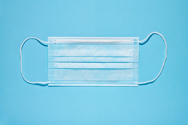 Top view of clean disposable face mask for medical use placed on blue background