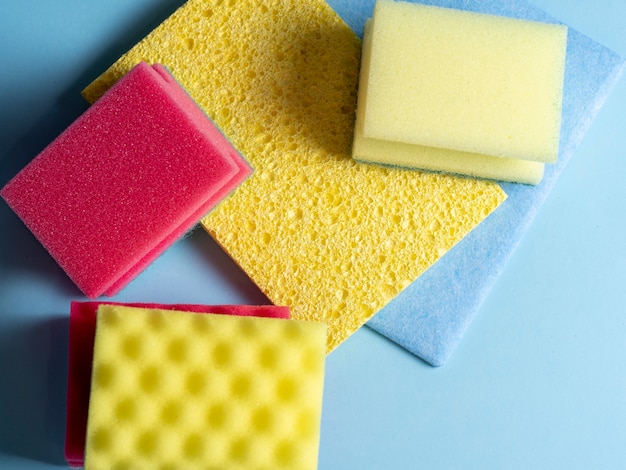 Top view of cleaning sponges of different colors and sizes laid out on a blue background