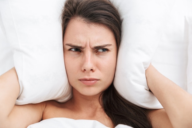 ベッドに横たわっている美しい若い女性の上面図、枕で耳を覆う