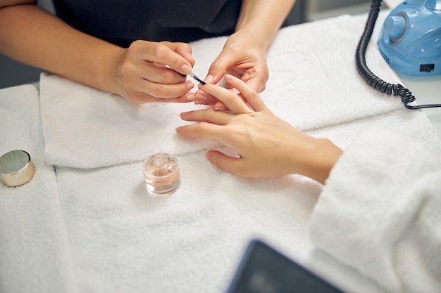 Top view close up of female hands while master is putting base on nails in salon