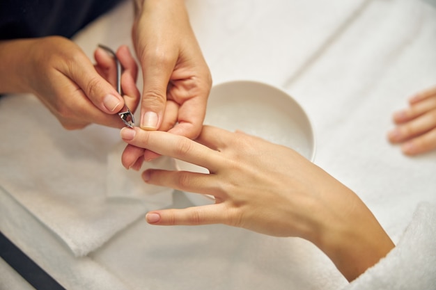 Top view close up of female hands while professional is removing cuticle above bowl with water