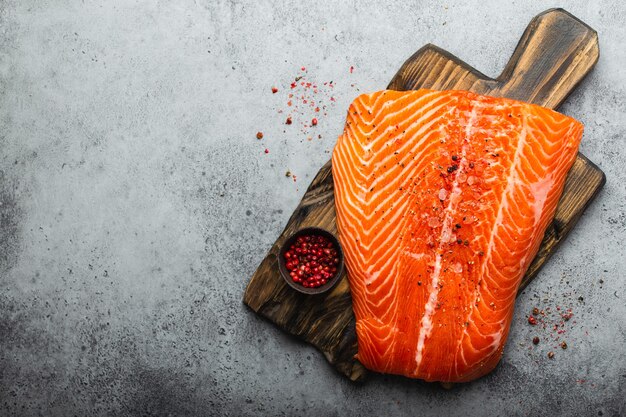 Top view, close-up of fresh raw salmon fillet with seasonings on wooden board, gray stone background. Preparing salmon fillet for cooking, healthy eating concept. Space for text