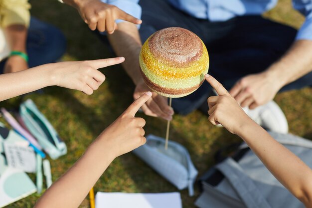 Top view close up of group of children pointing at model planet while enjoying outdoor astronomy class in sunlight, copy space