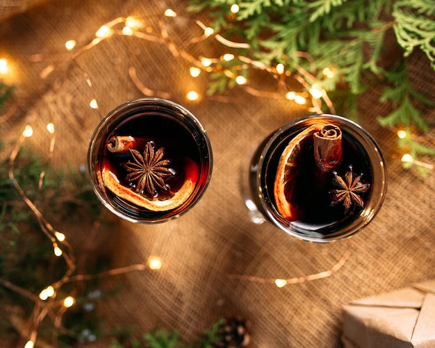 Top view close up on mugs of glintwine with fir branches and garland lights on the wooden table