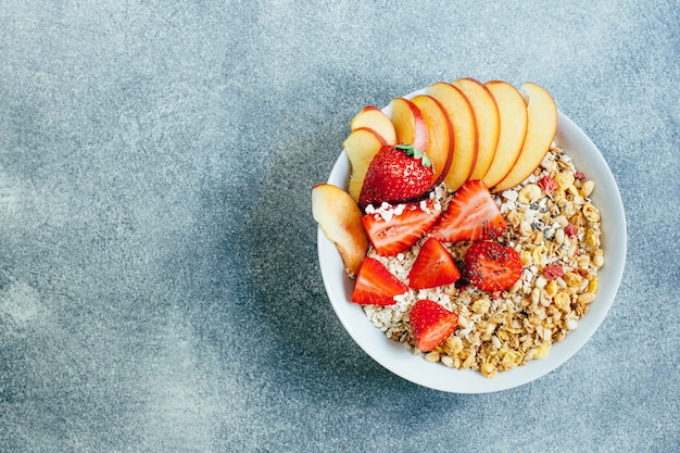 Top view close-up of porridge granola oatmeal with strawberry peach dried fruits in a white round plate on a gray background