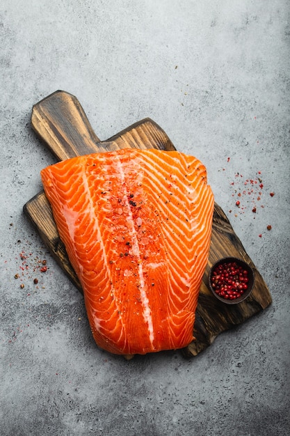 Top view, close-up of whole  fresh raw salmon fillet with seasonings on wooden board, gray stone background. Preparing salmon fillet for cooking, healthy eating concept