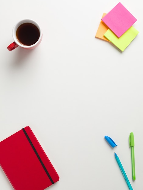 Top view of a closed red notebook, colored reminders, blue and green pen,