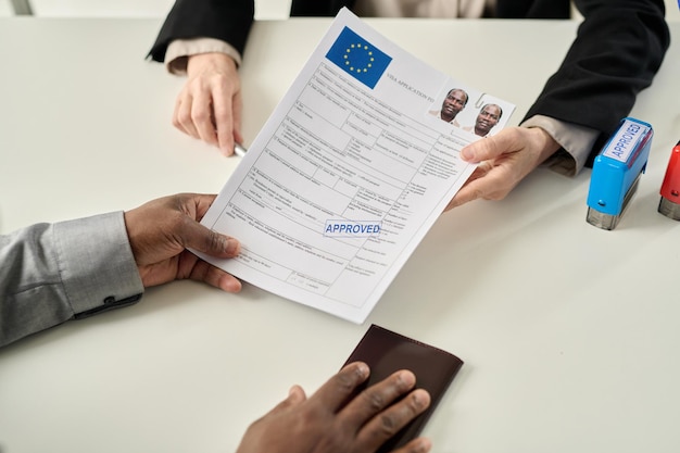 Top view closeup of black man holding approved visa application form in immigration office