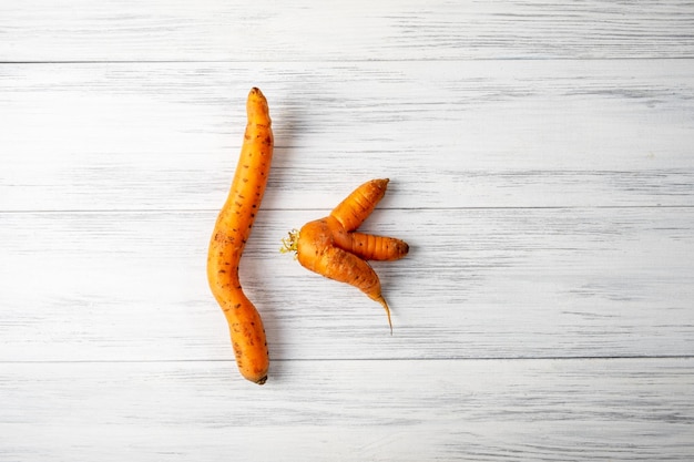 Top view closeup of two ripe orange ugly carrots lie on a light wooden surface with copy space for
