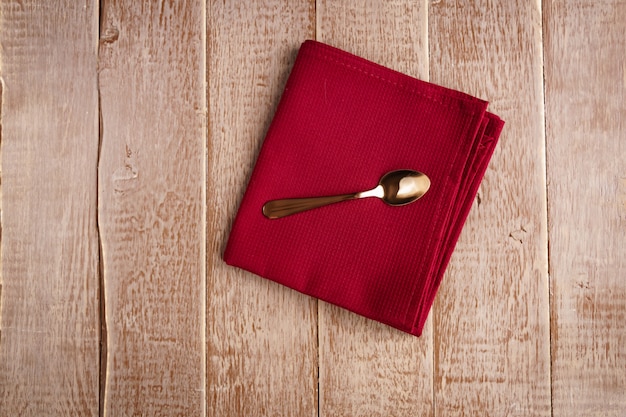 Top view of cloth napkin of beige color and served tea spoon on wooden table.