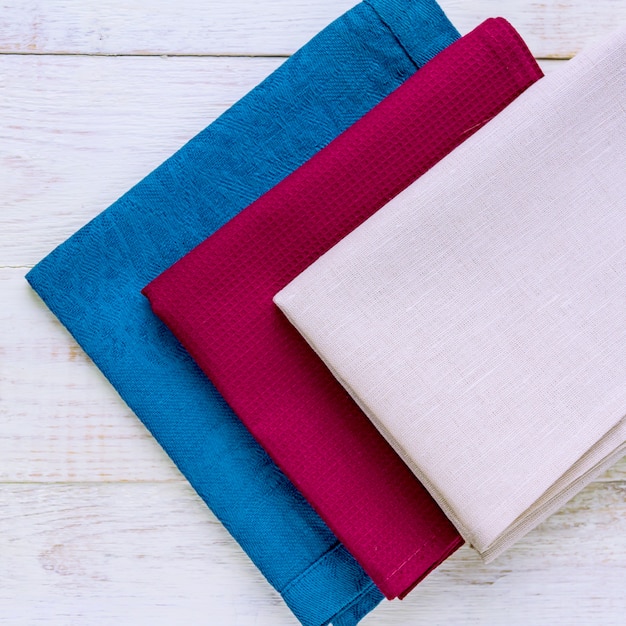 Top view of cloth napkins of beige, blue and burgundy colors on rustic white wooden background.