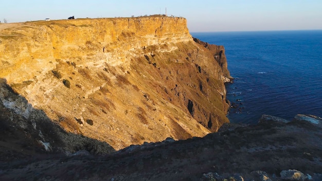 Top view of coastal cliff with blue sea at sunset