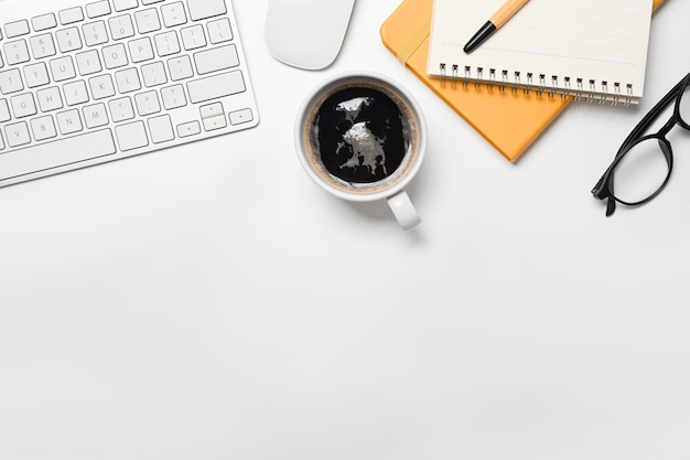 Top view coffee cup eyeglasses notebook and wireless keyboard on white table Copy space