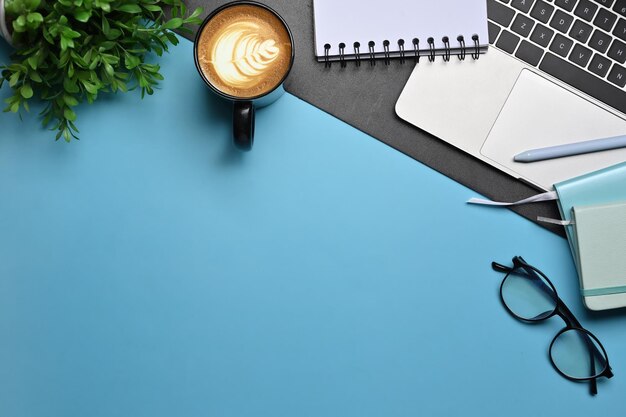 Top view coffee cup glasses notebook and computer laptop on blue background