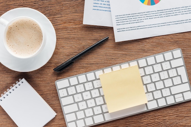 Top view of coffee cup keyboard and papers on wooden background