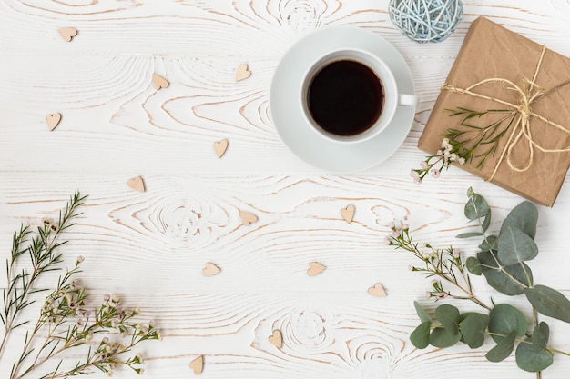 Top view of coffee, gift wrapped in kraft paper , hearts, flowers on white wooden table. Background with free space for text. Flat lay.