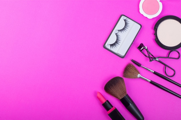 Top view of A collection of cosmetic beauty products arranged around a blank space on a pink background.