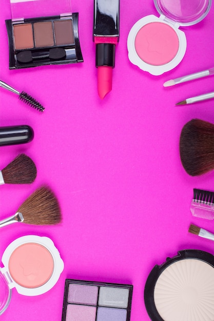 Top view of A collection of cosmetic beauty products arranged around a blank space on a pink background.