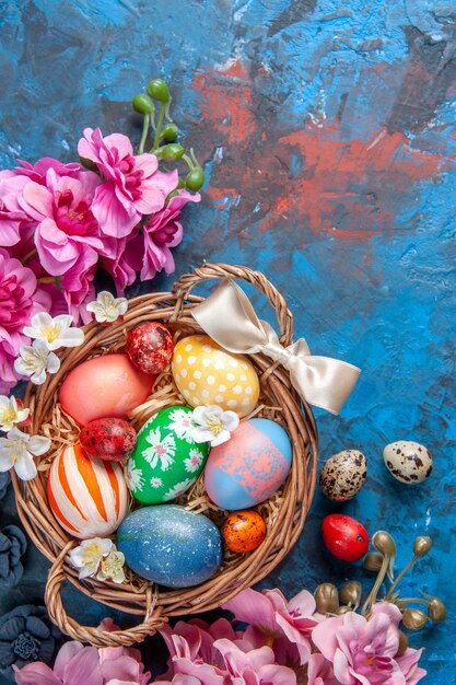 Vista dall'alto uova di pasqua colorate all'interno del cesto con fiori su superficie blu