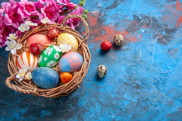 top view colored easter eggs inside basket with flowers on blue surface