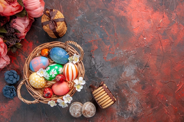 top view colored easter eggs inside basket with flowers on dark surface