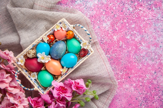 Vista dall'alto uova di pasqua colorate all'interno di una graziosa scatola con fiori sulla superficie rosa colore primaverile colorate vacanze di pasqua concetto ornato