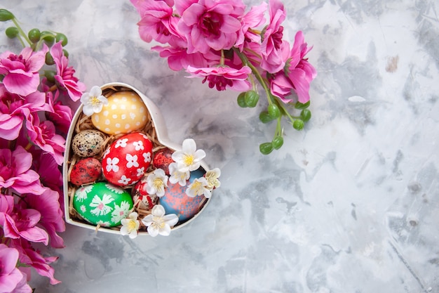 вид сверху цветные пасхальные яйца внутри коробки в форме сердца с цветами белая поверхность концепция праздника пасха весна богато украшенный красочный