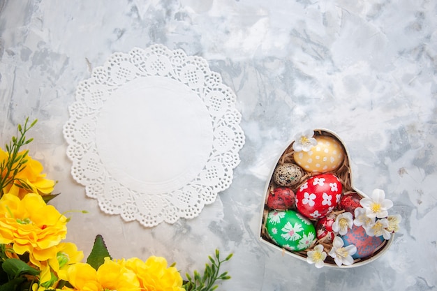 Top view colored easter eggs inside heart shaped box with yellow flowers white surface spring holiday easter ornate colourful concept