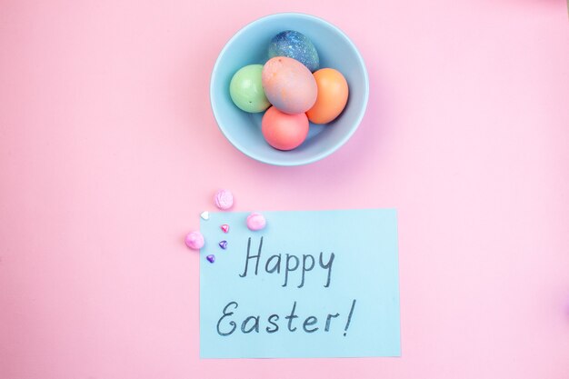 top view colored easter eggs inside plate with happy easter note on pink surface