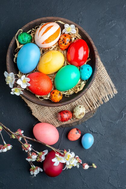вид сверху цветные пасхальные яйца внутри тарелки с соломой на темной поверхности