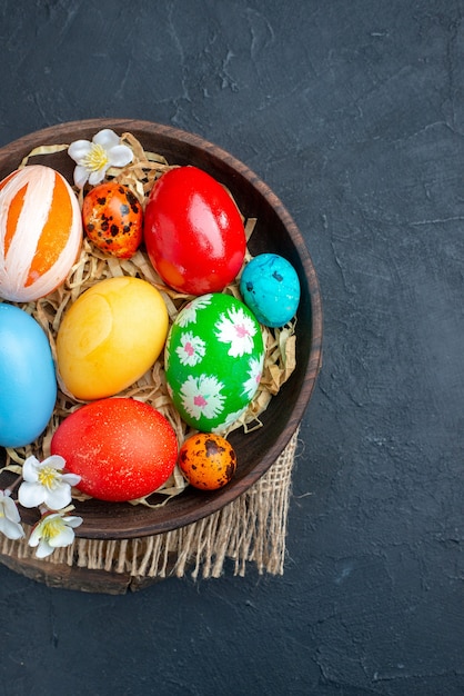 top view colored easter eggs inside plate with straw on dark surface