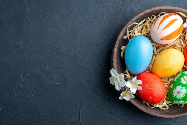 top view colored easter eggs inside plate with straw on dark surface