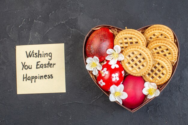 top view colored easter eggs with cookies inside heart shaped box on dark surface