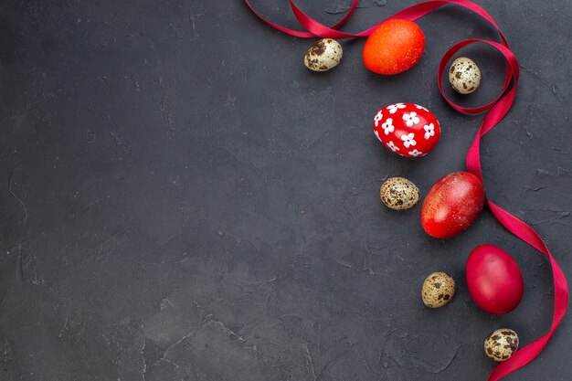 top view colored easter eggs with quail eggs and red bow on dark surface