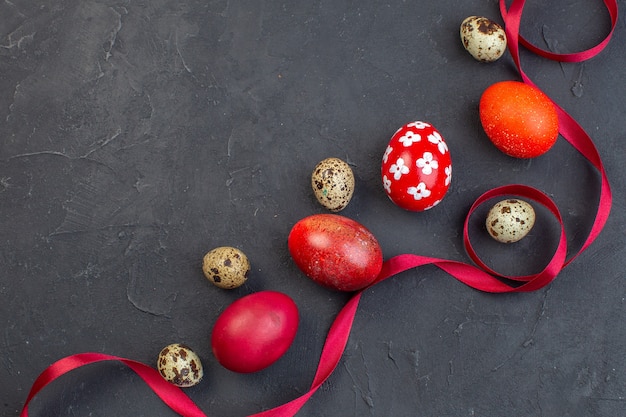 top view colored easter eggs with quail eggs and red bow on dark surface