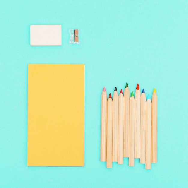 Top view of colored pencils and yellow color sketch pad for creativity. Set of wooden multicolored pencils, pencils sharpener, eraser. Design background social media.