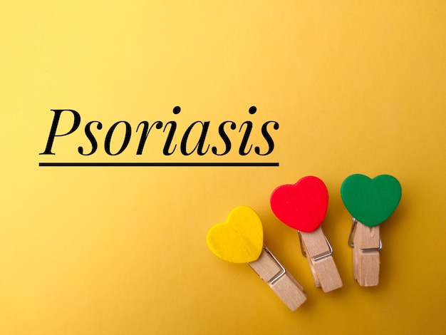Photo top view colored wooden clips with text psoriasis on yellow background