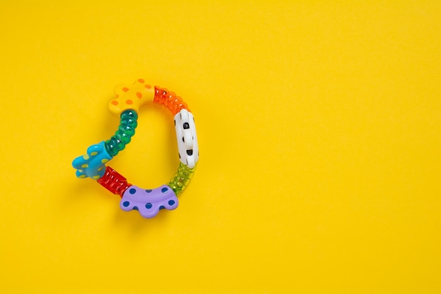 Top view a colorful baby rattle on yellow background with copy space