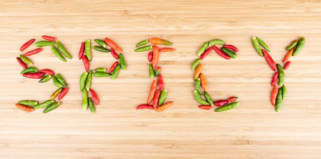 Top view colorful bird chilli with message SPICY on wooden background