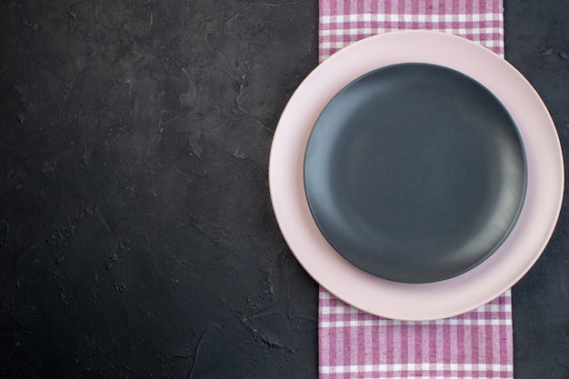 Top view of colorful ceramic empty plates on pink stripped towel on black background with free space