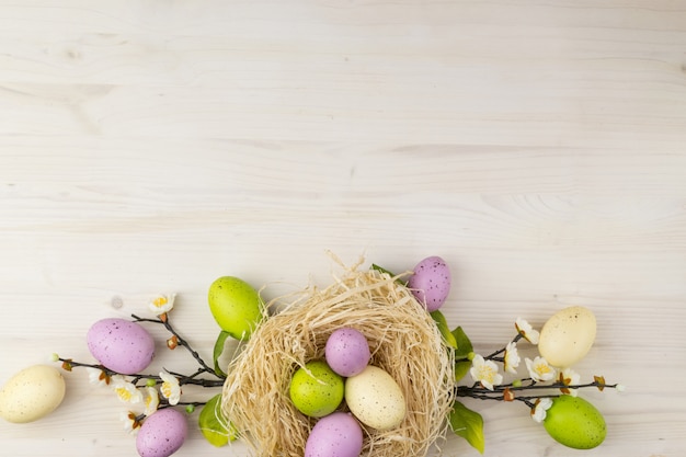 Photo top view of a colorful easter eggs in nest and  spring flowers on a light wood background with message space.