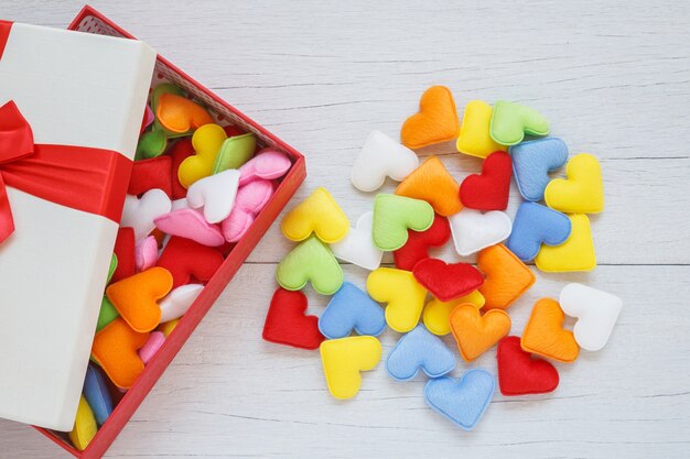 Top view colorful heart shape in gift box with ribbon on white wooden plank background